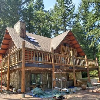 Log cabin with brown roof and wood railing, surrounded by trees.