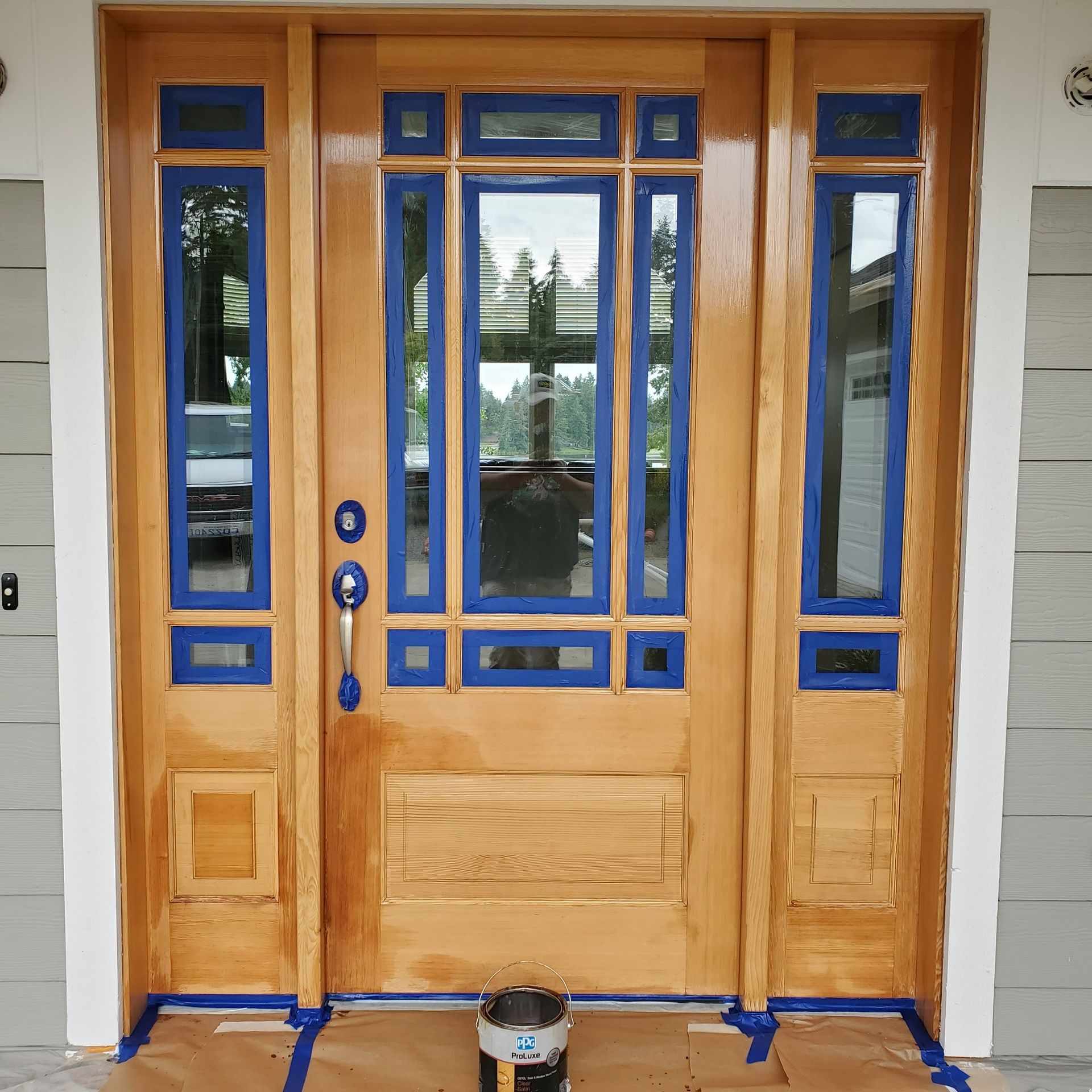 Wooden front door with blue painter's tape, ready to be painted. Door features glass panes and sidelights.