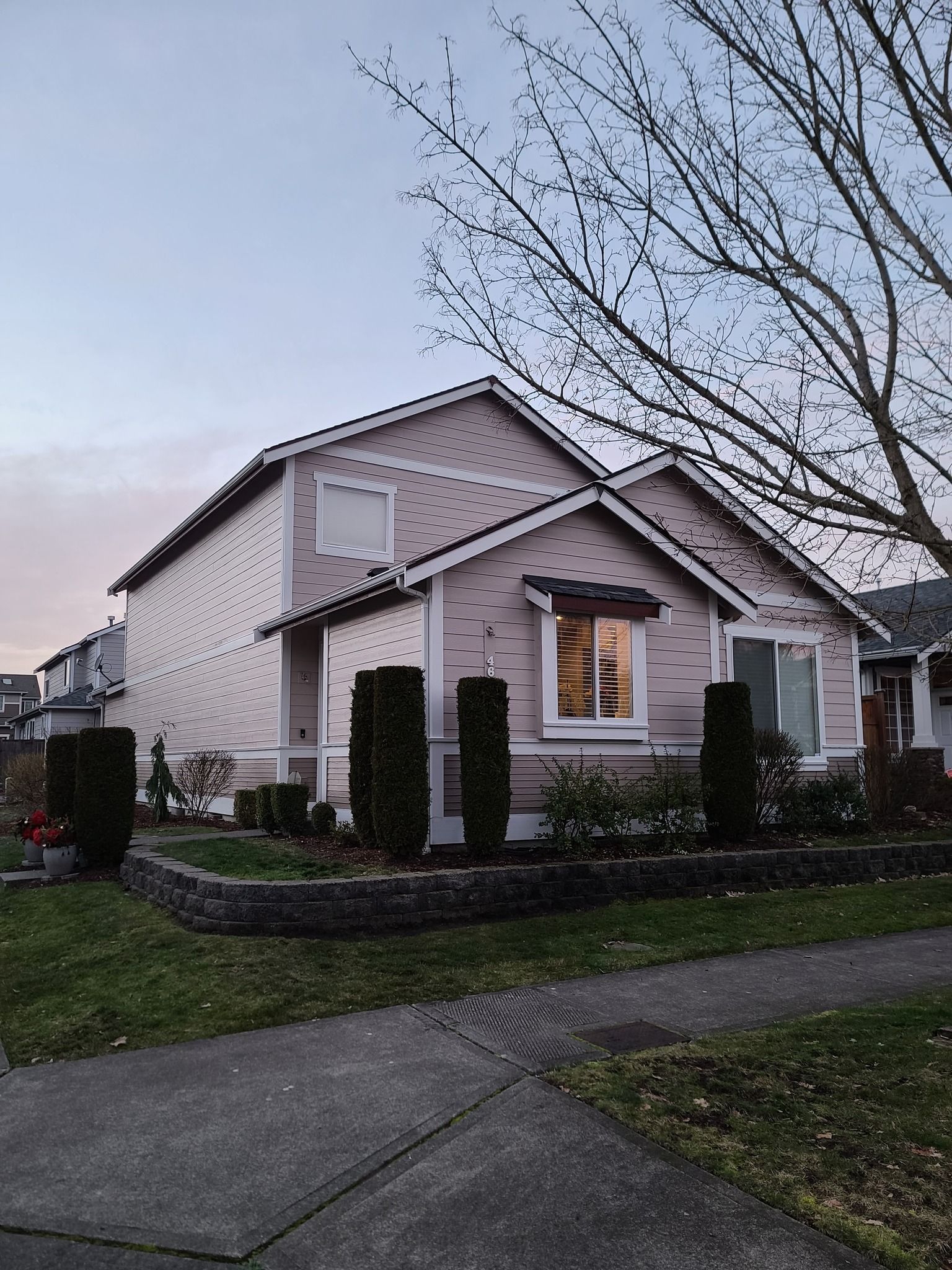 Two-story house with light pink siding, small rectangular bushes, and a sidewalk in front.