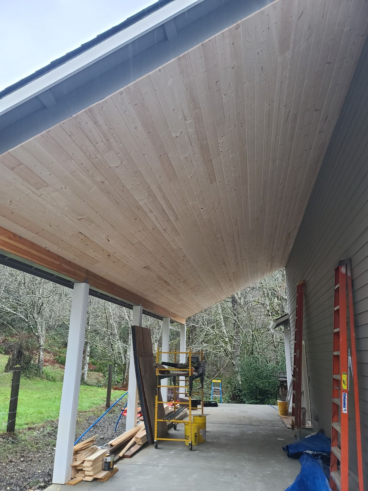 Newly installed wooden porch ceiling; construction tools, ladders, and materials visible.