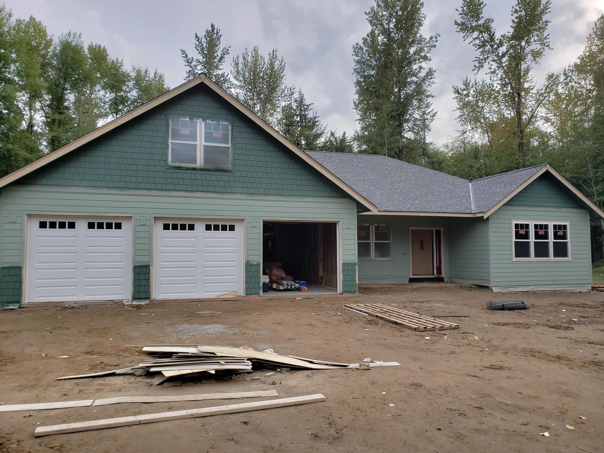 New house under construction; green siding, white garage doors, and unfinished driveway.