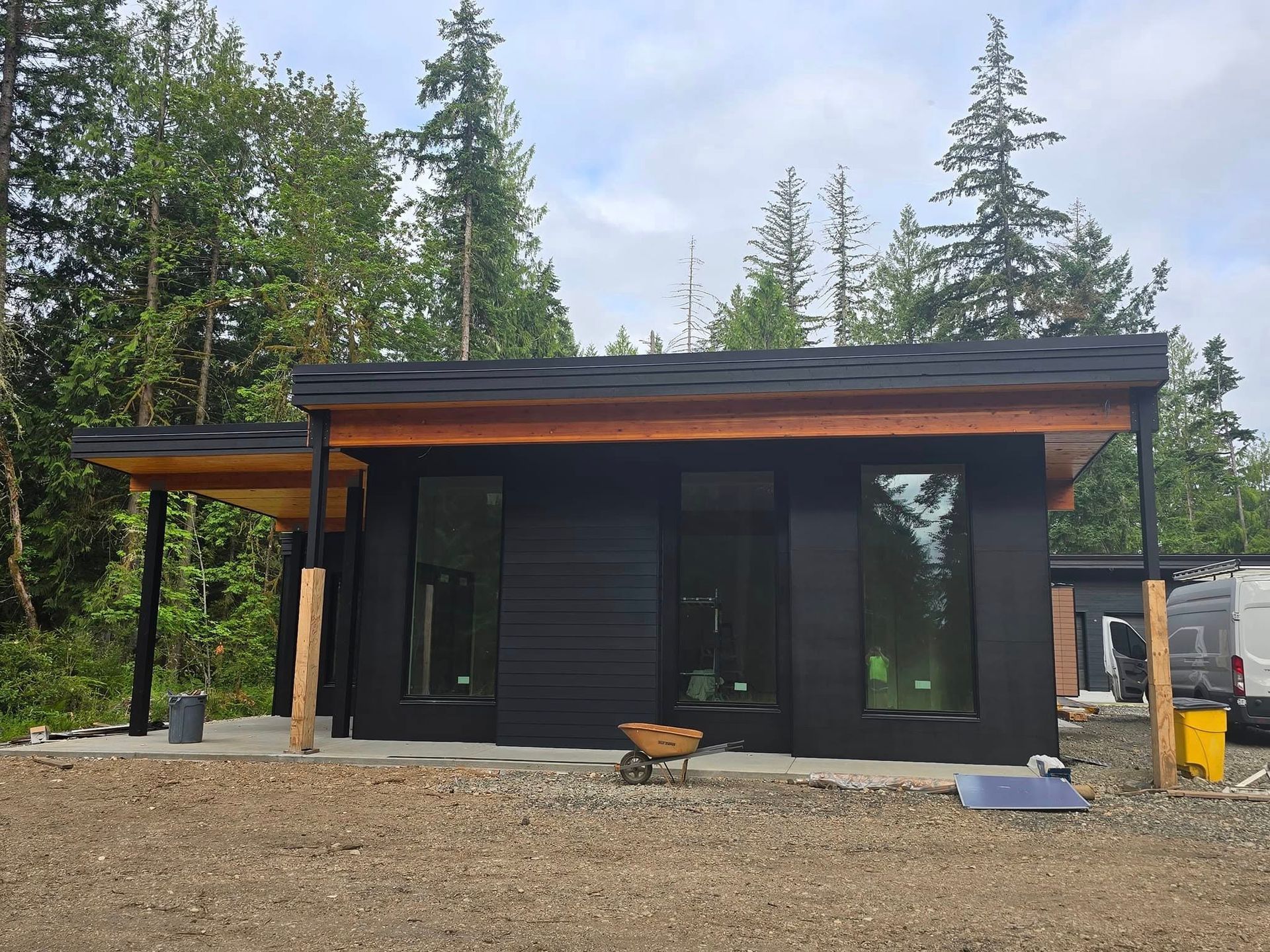 Black cabin with large windows and a covered porch in a wooded area.