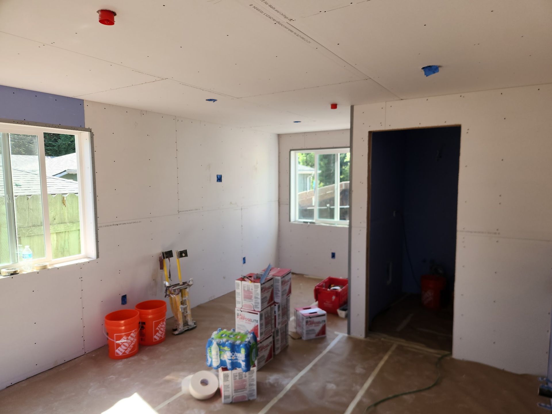 Interior room under construction, drywall installed. Orange buckets and building supplies present.