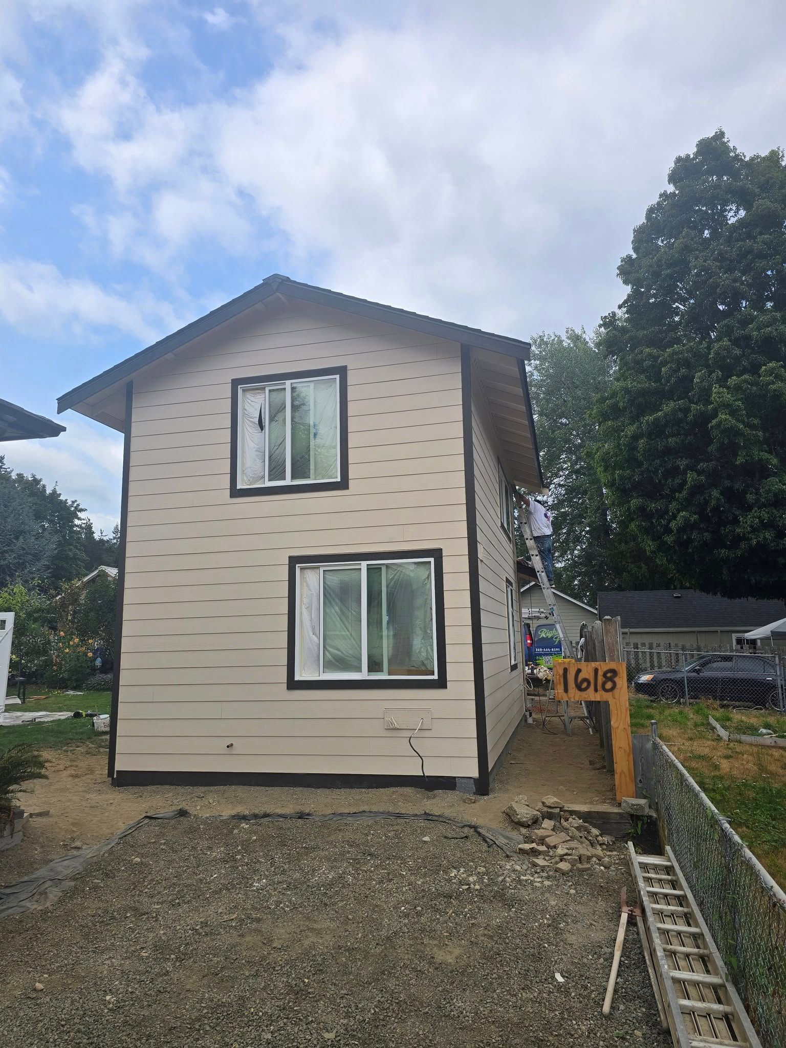 Two-story house with tan siding, black trim, and windows under a cloudy sky.