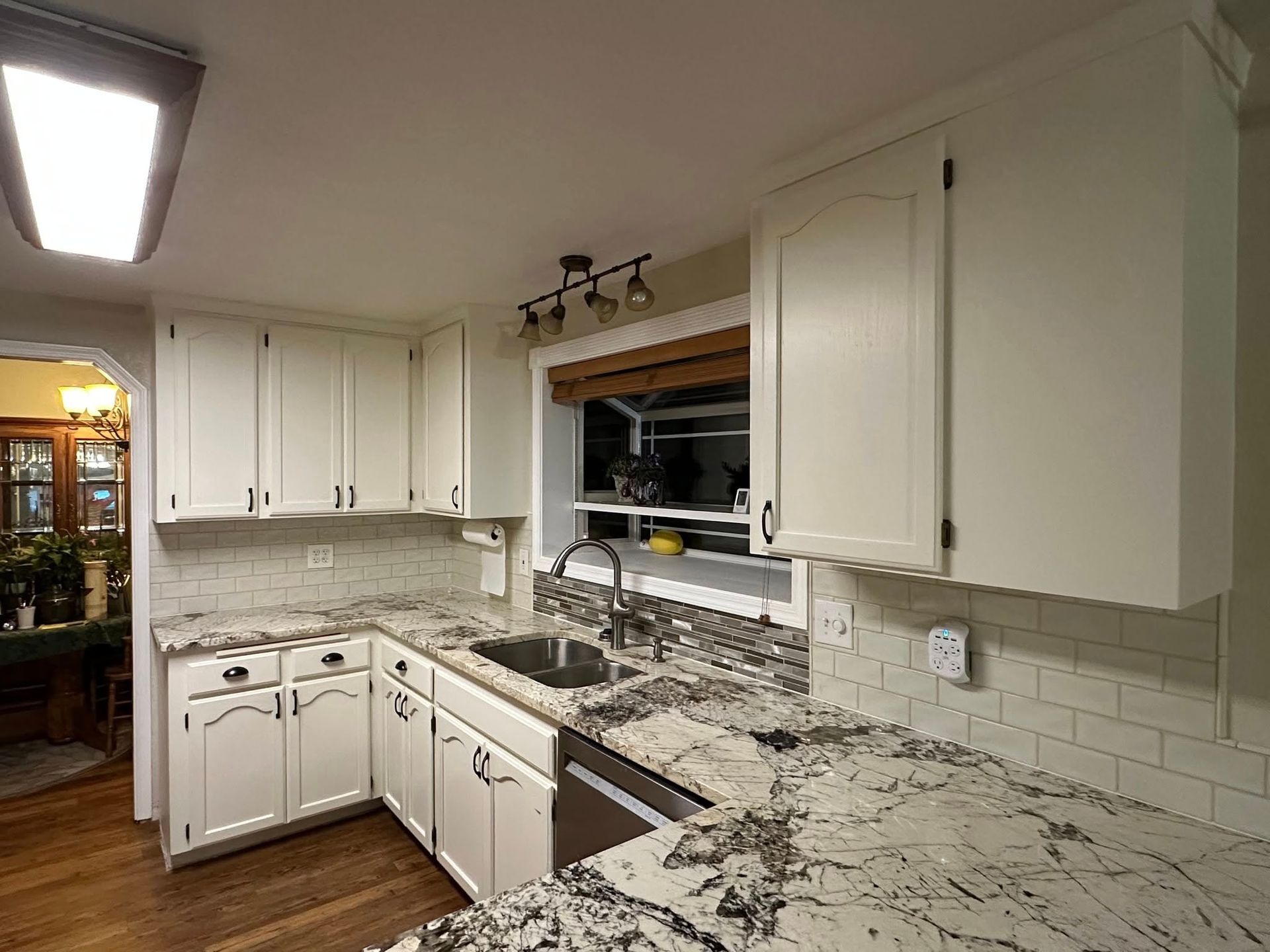 White kitchen with granite countertops, cabinets, and a sink beneath a window.