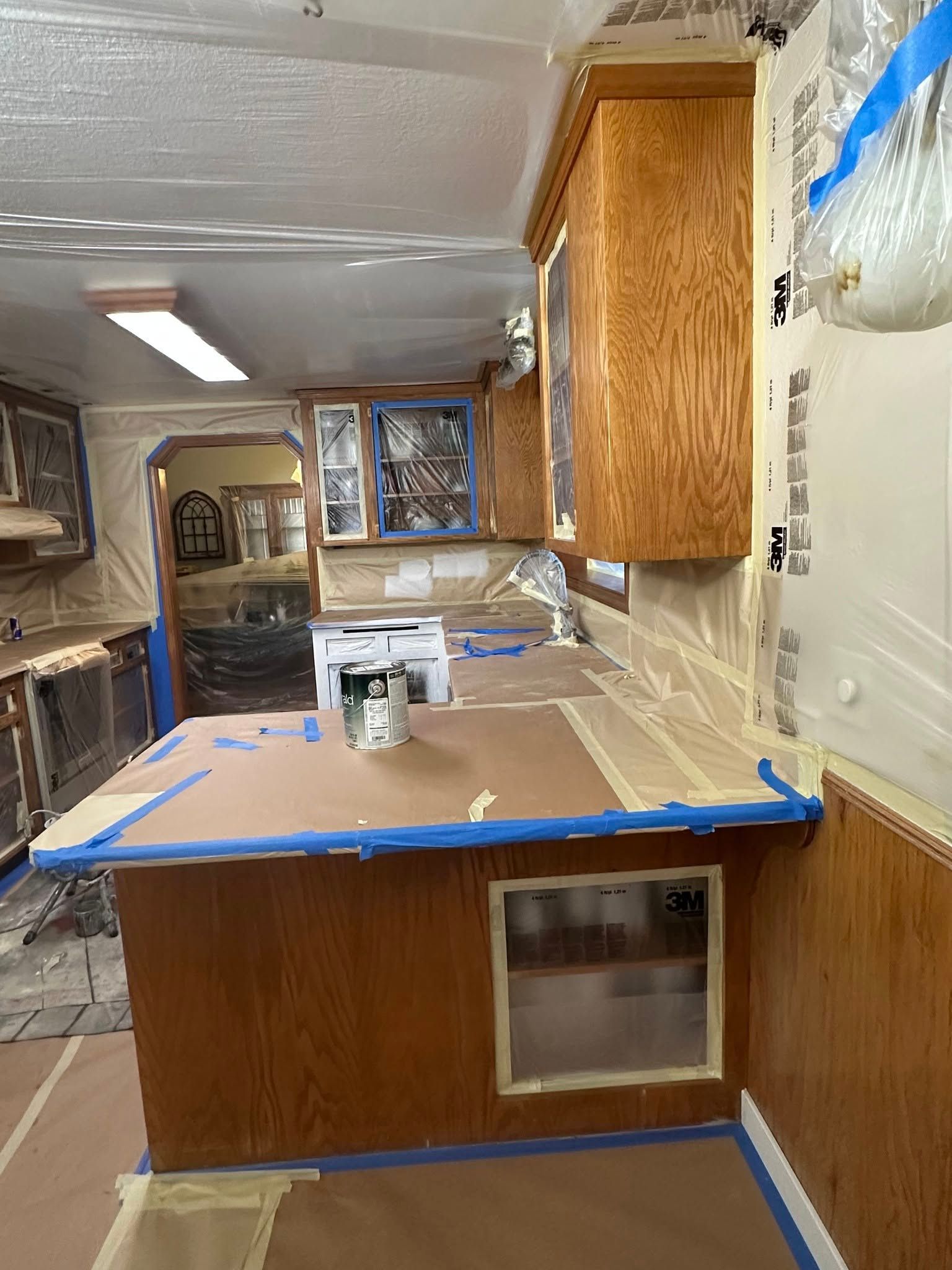 Kitchen being prepped for painting: cabinets and surfaces masked with tape and plastic.