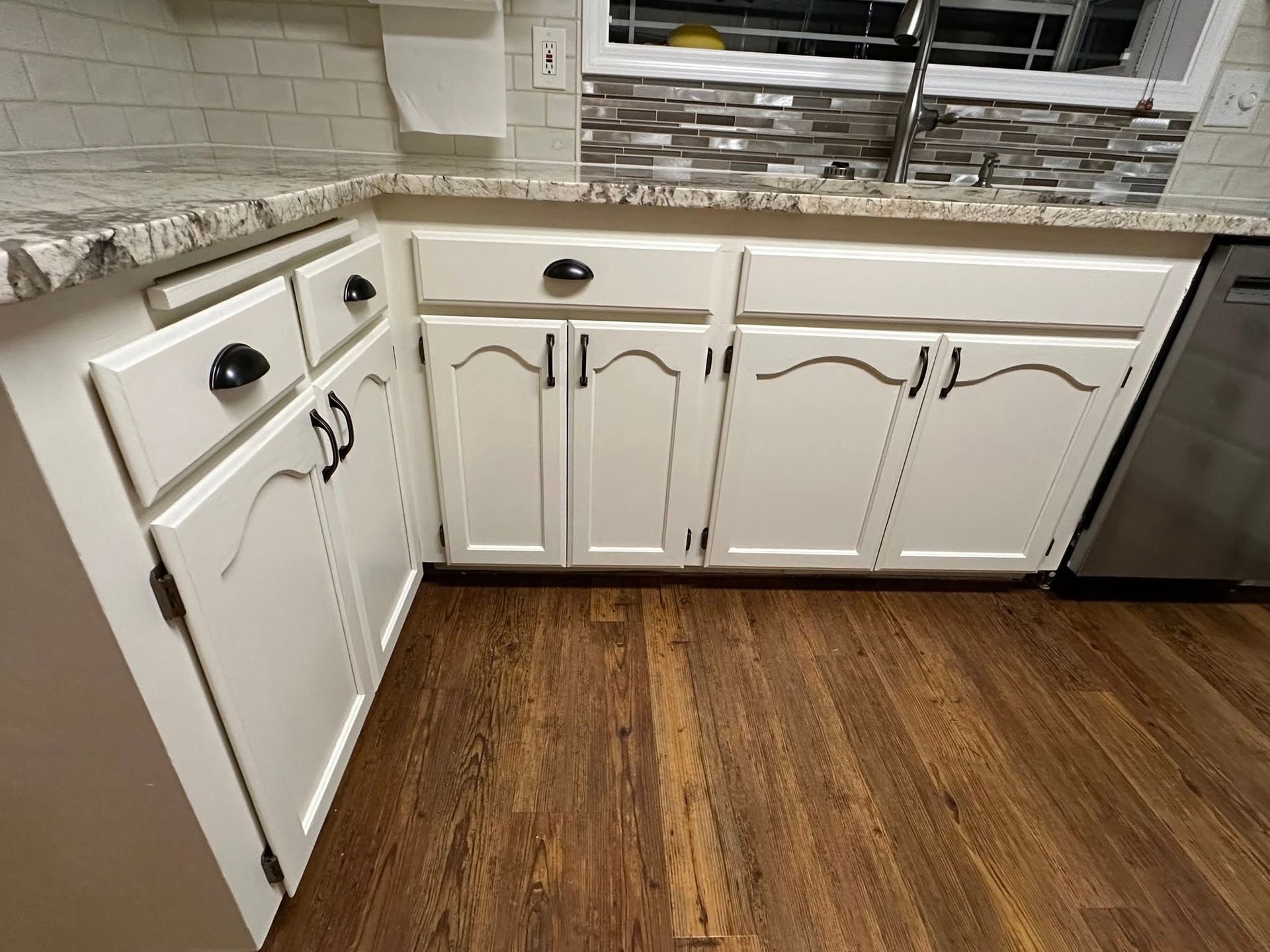 White kitchen cabinets with black hardware and wooden floor.