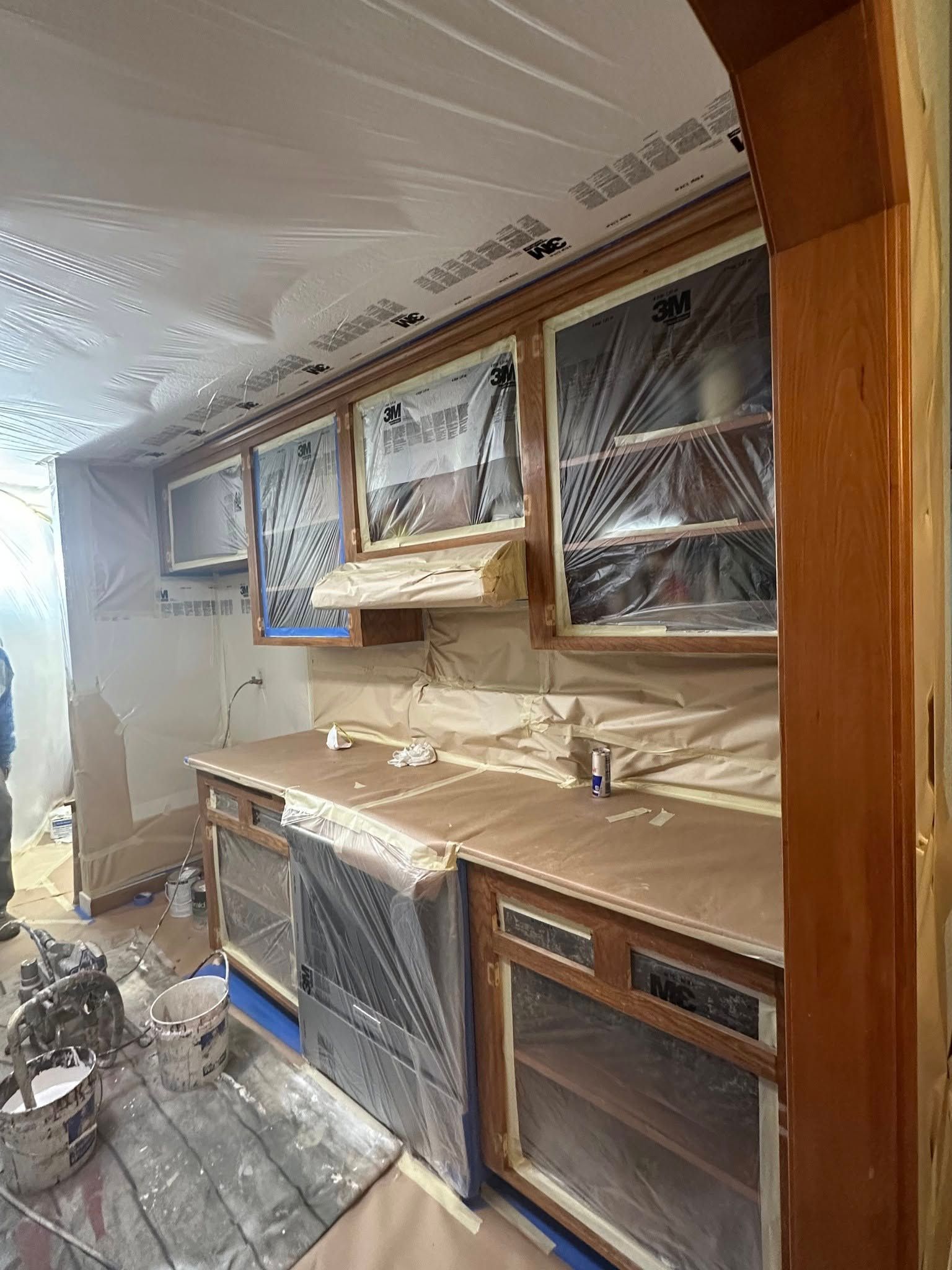 Kitchen cabinets and appliances covered in plastic, prepared for painting.