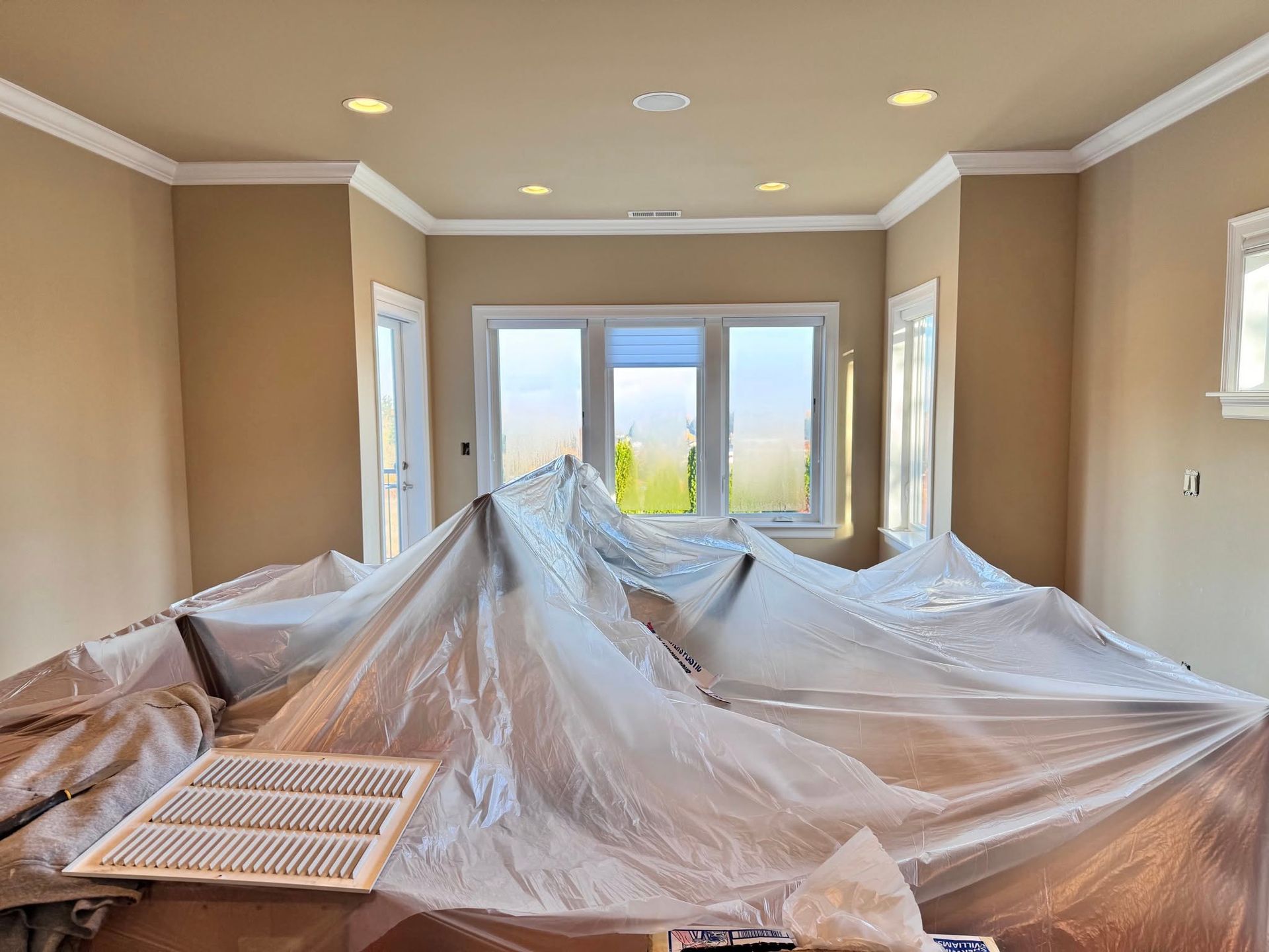 Room with painted beige walls, white trim, and a window; furniture covered in plastic.