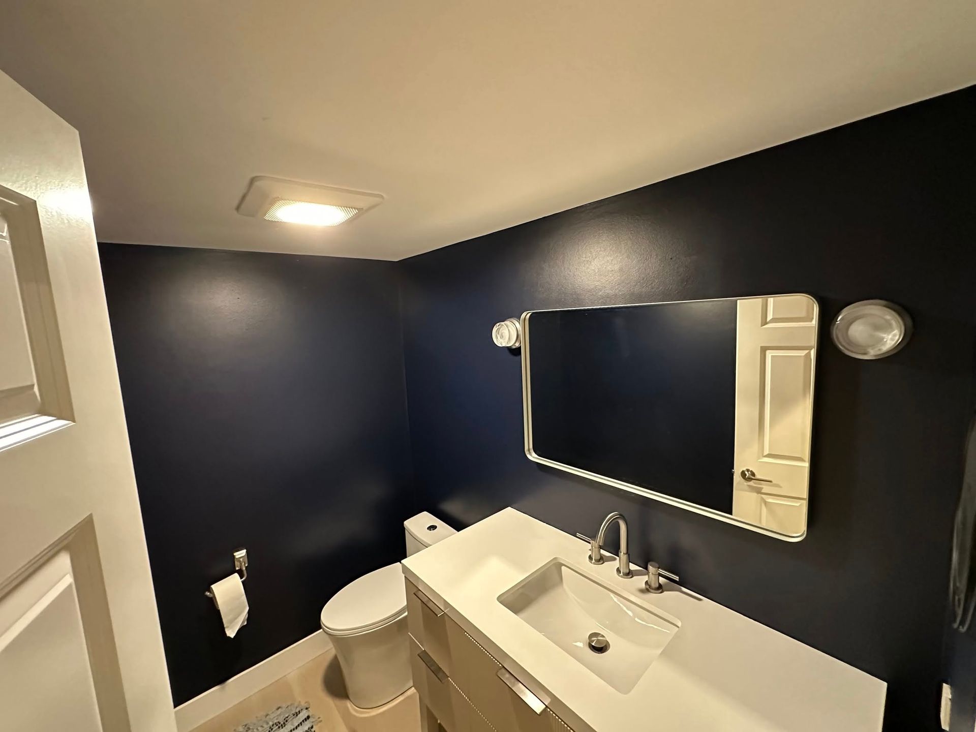 Small bathroom with dark blue walls, white sink, toilet, and mirror.