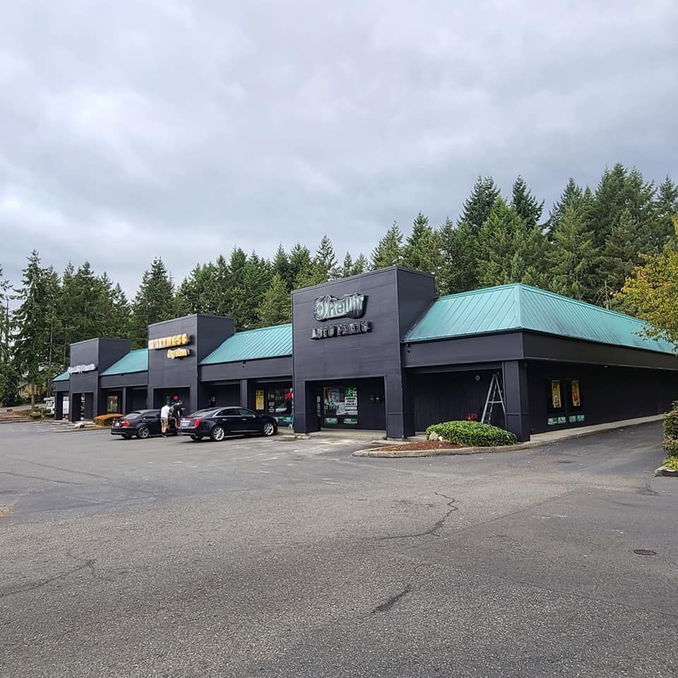Exterior of a strip mall with black buildings, green roofs, and parking lot under a cloudy sky.