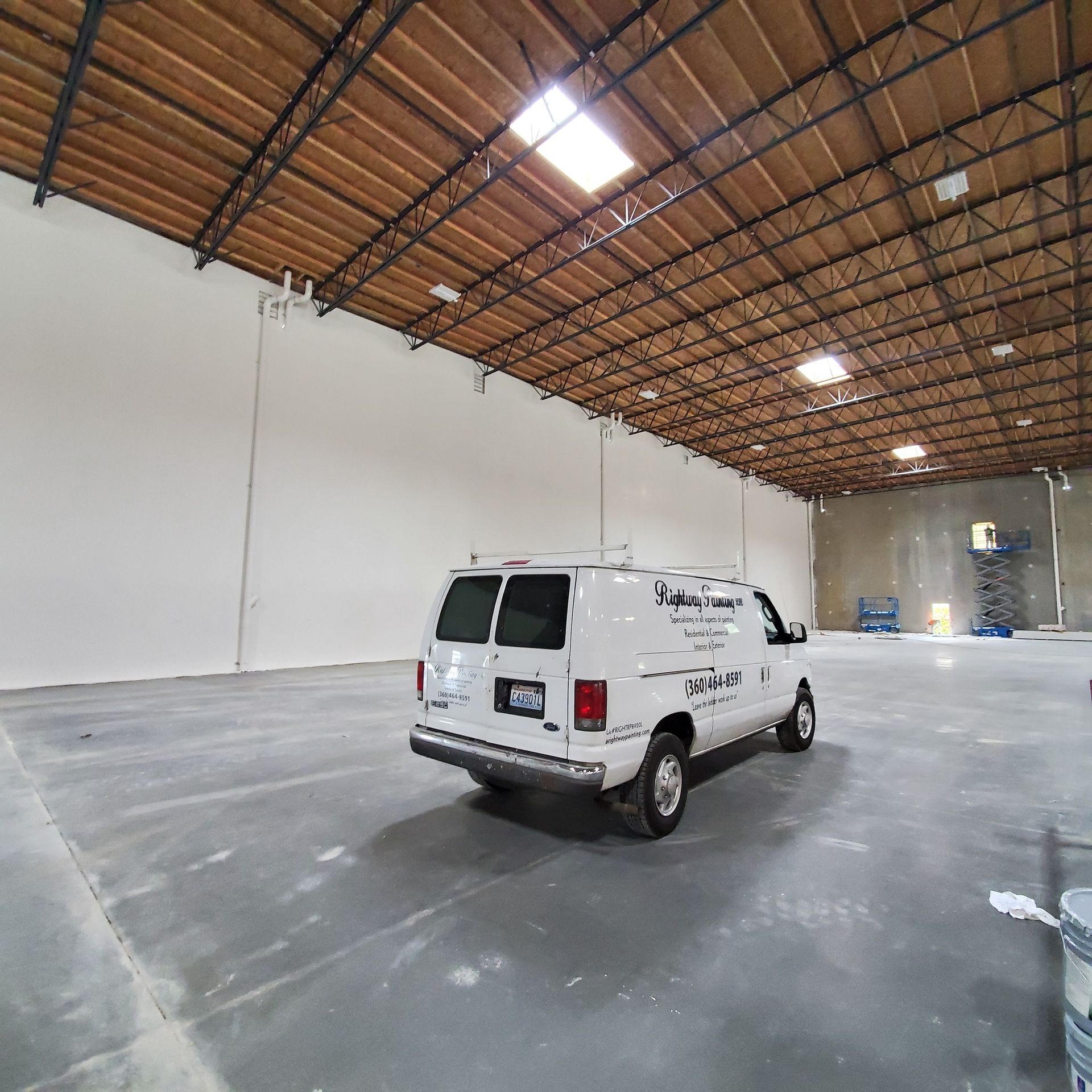 White van in a large empty warehouse with high ceiling and skylights.