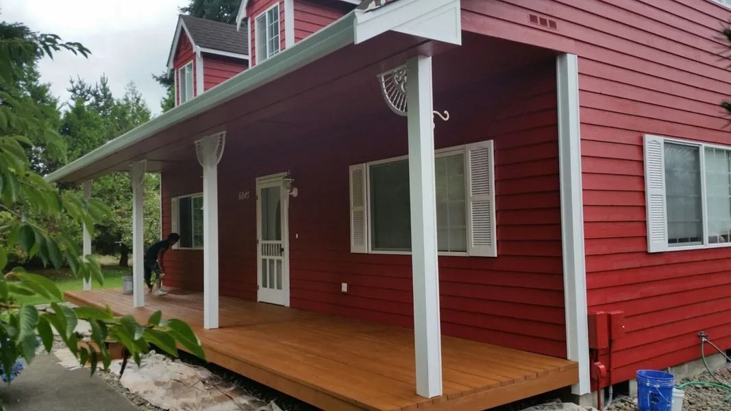 Red house with a porch and white pillars. A person stands on the porch.
