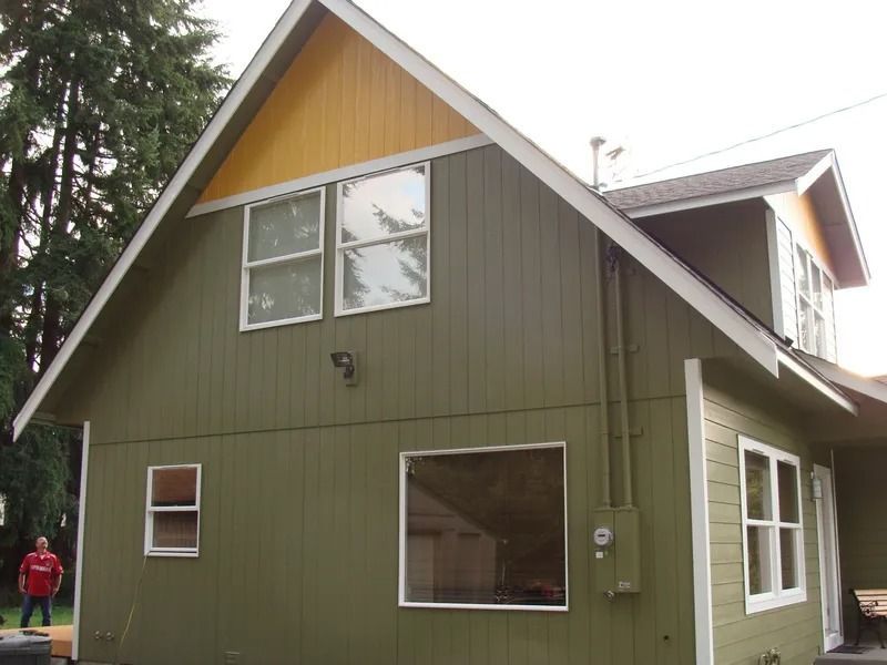 Green house with yellow gable, white-framed windows, and a person in red shirt.
