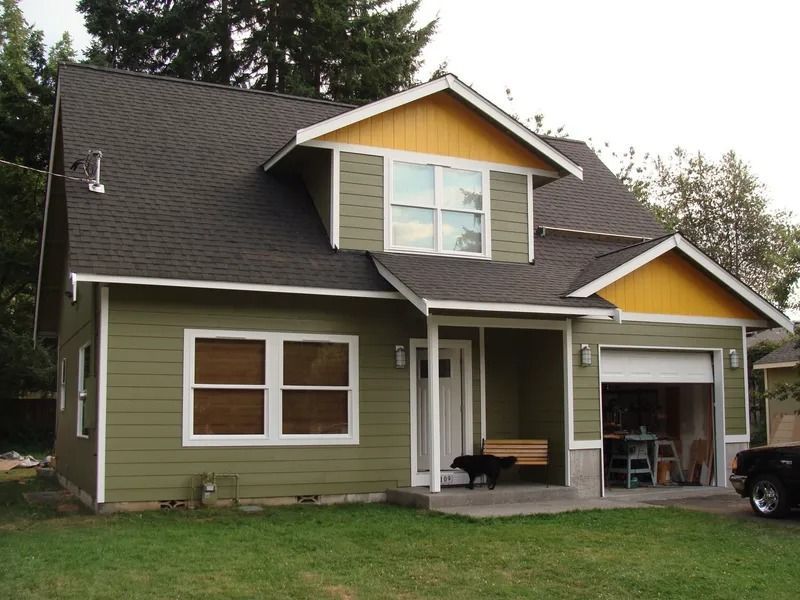Two-story house with green siding, yellow trim, and a garage. A dog sits on the porch.