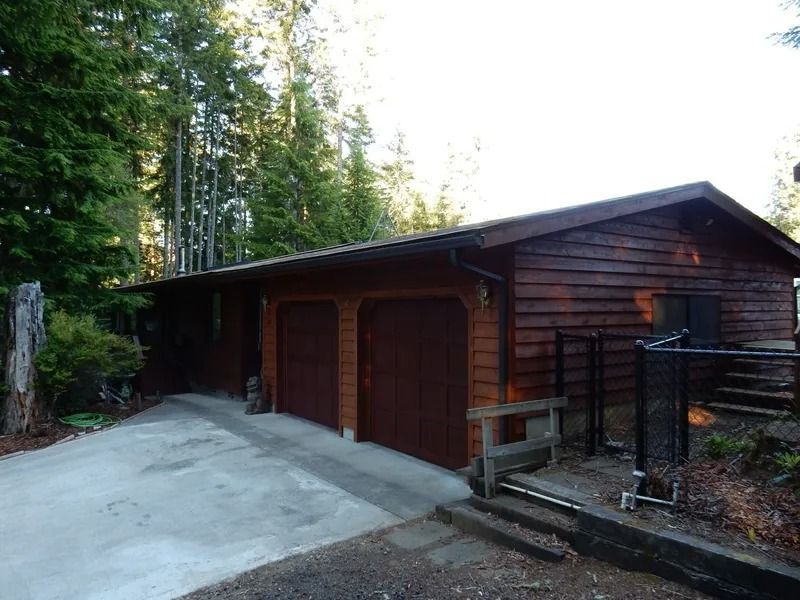 Brown cabin with a two-car garage, driveway, and surrounding trees.