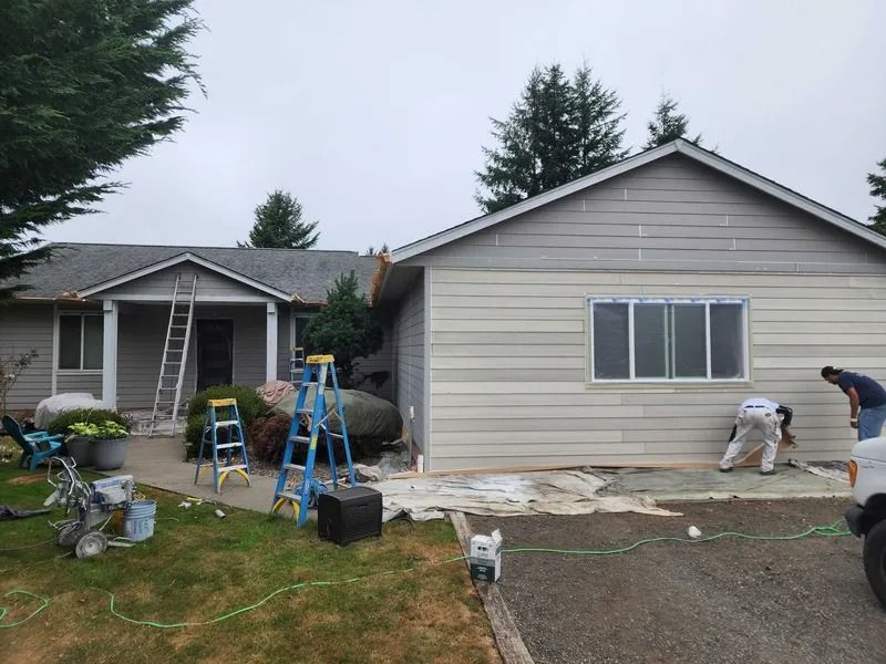 House exterior being painted; two workers applying paint, one on the ground, another on a ladder.