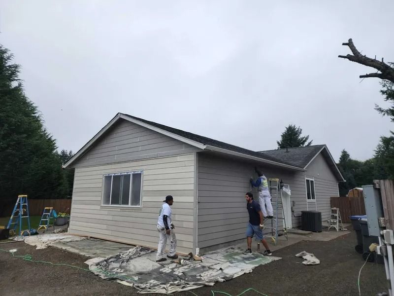 Workers painting the exterior of a house on an overcast day.