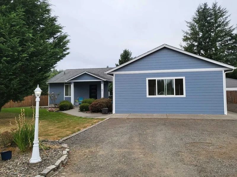 Blue house with attached garage, gravel driveway, and a white lamp post on the lawn.