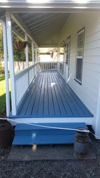 Blue-painted porch with white railing on a white house. A milk can sits nearby.