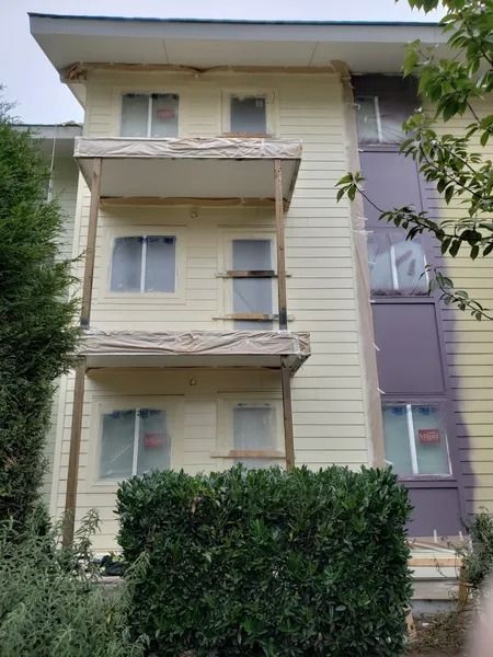Building exterior being painted, scaffolding in place. Yellow siding, purple accent, tarp-covered windows.