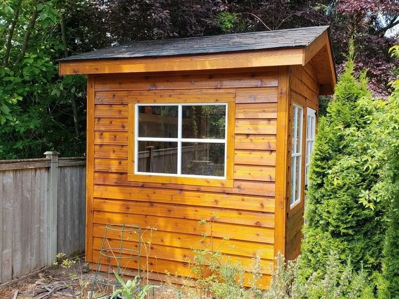 Small wooden shed with a window, in a garden.