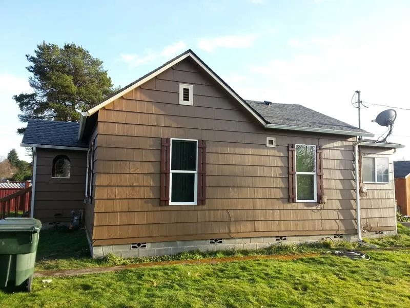 Brown-sided house with a gable roof, two windows with red shutters, and a satellite dish.