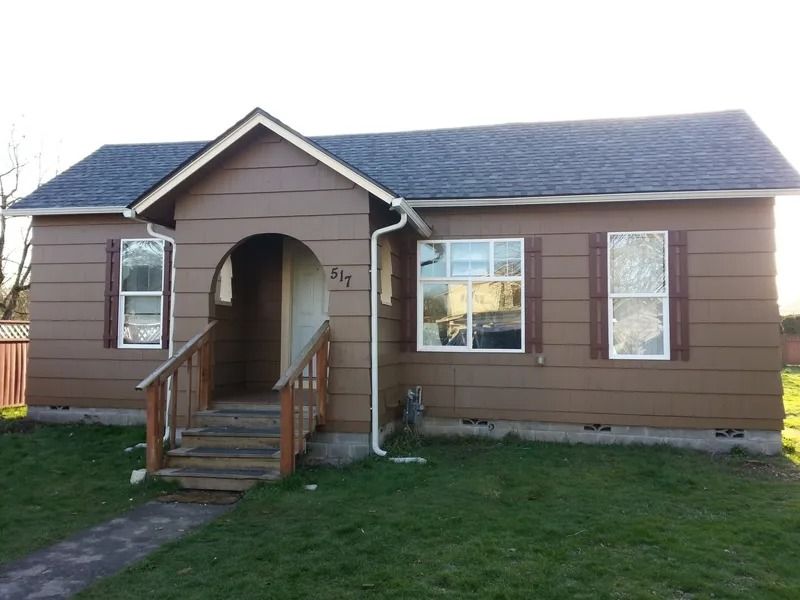 Brown house with white-framed windows, brown shutters, arched entryway, and dark roof. Green lawn in front.