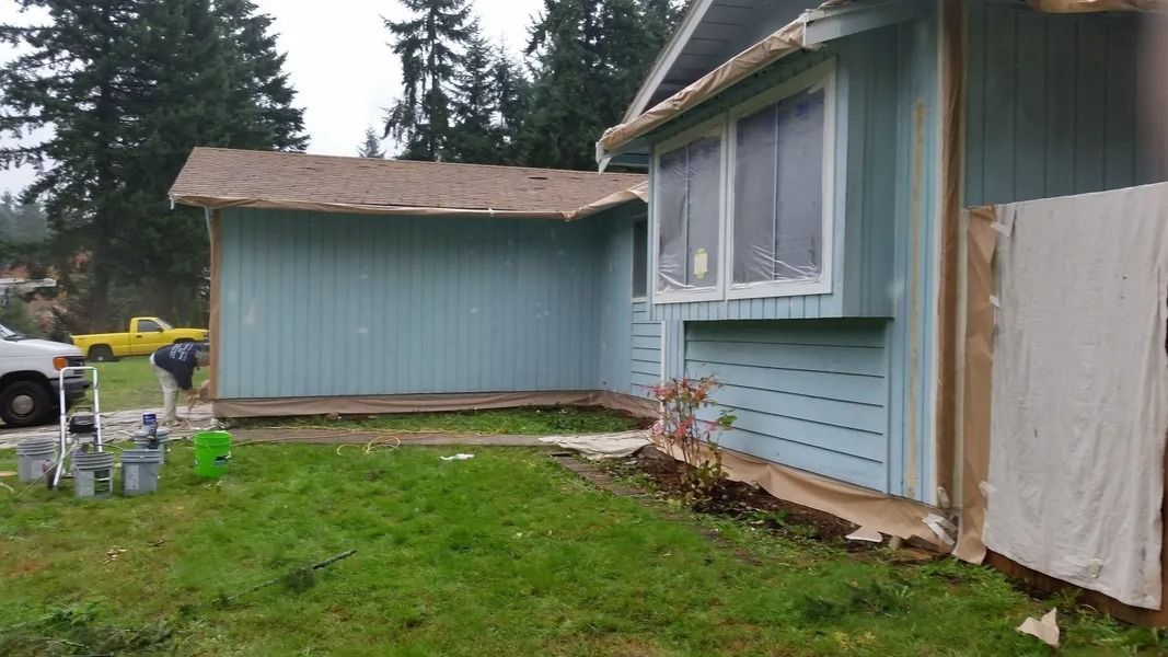 Blue house with peeling paint, overgrown lawn, and a small outbuilding.