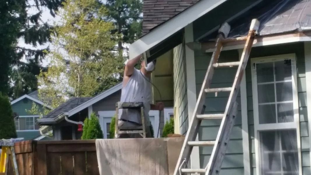 Person on ladder paints exterior trim of a house.