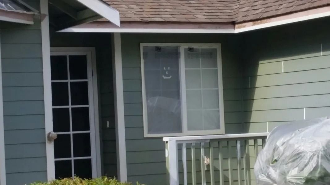 Green house exterior with white door, window, and railing. Brown roof, sunny.