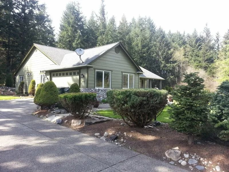 Green house with a driveway and surrounding greenery.