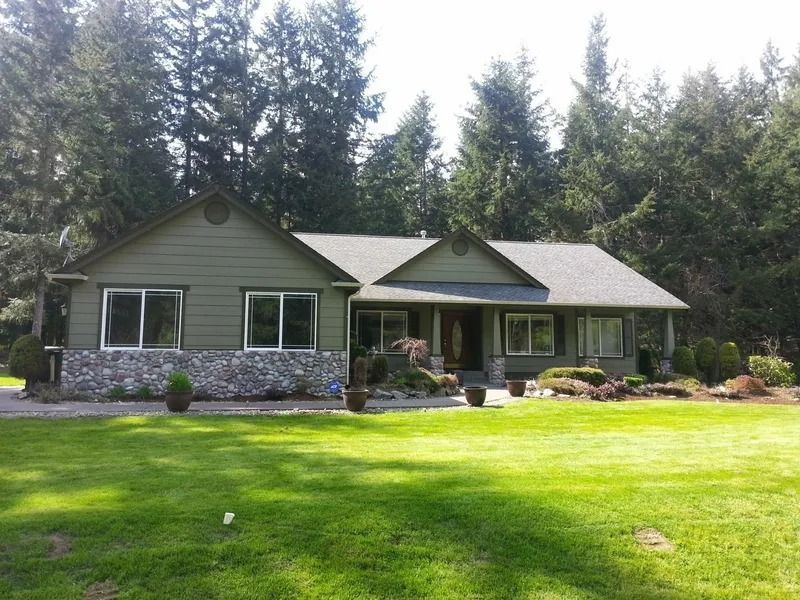 Green ranch-style house with stone accents, green lawn, and tall trees in the background.