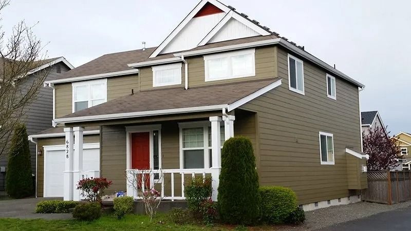 Two-story house with green siding, white trim, red front door, and a small porch on a cloudy day.
