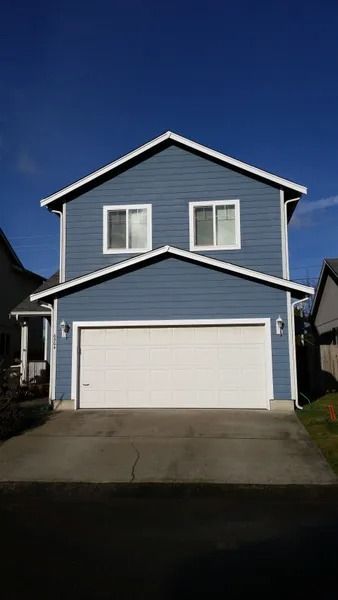 Blue two-story house with white trim and a two-car garage under a bright blue sky.