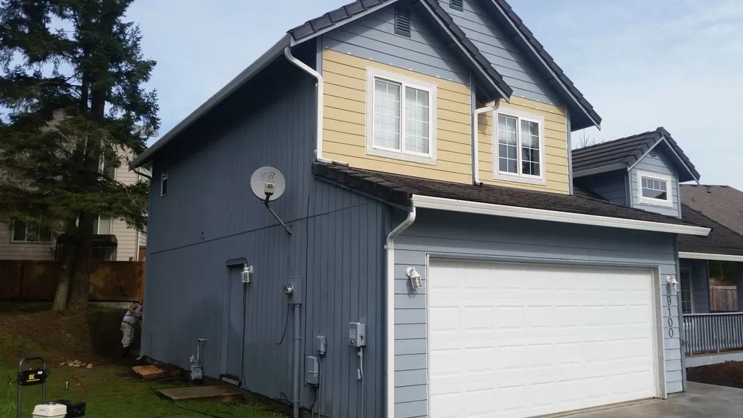 Blue and tan two-story house with a white garage door, white windows, and brown roof.
