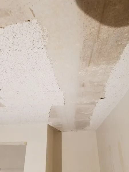 Ceiling with water damage and peeling paint, above a white wall in a corner.