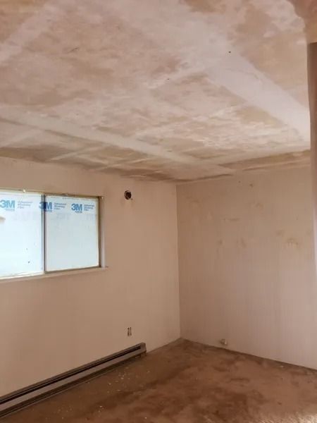 Empty room with peeling ceiling, boarded window, and brown floor.