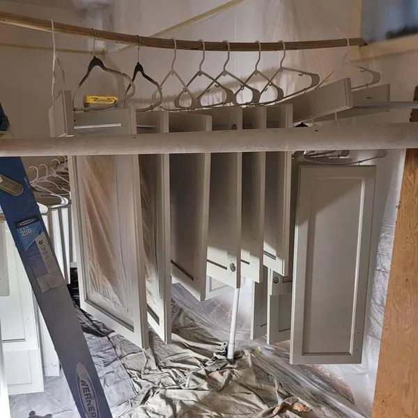 White cabinet doors hanging to dry in a makeshift painting area, covered with plastic.