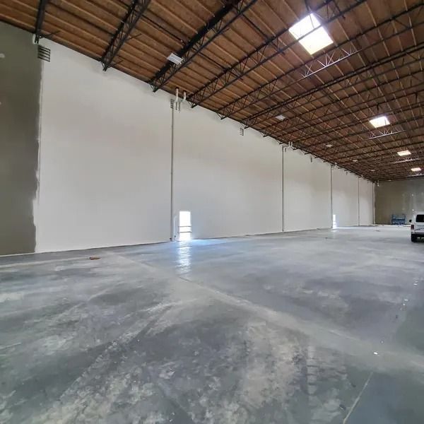 Empty warehouse interior with concrete floor, white walls, and exposed ceiling beams.