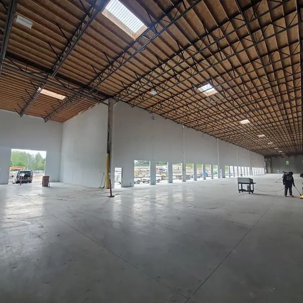 Large, empty warehouse interior with high ceilings, skylights, and concrete floor.