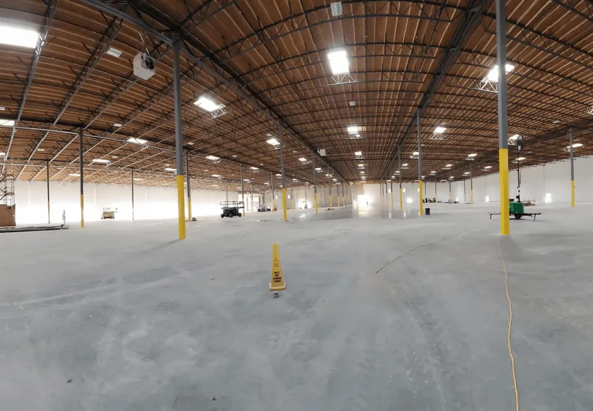 Wide shot of an empty warehouse with a high ceiling, concrete floor, and yellow support poles.