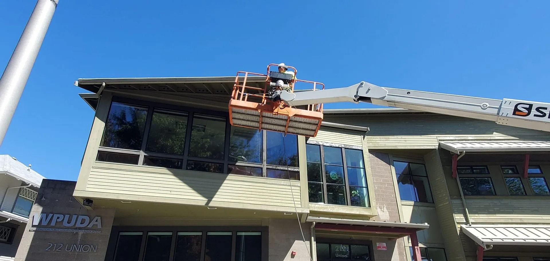 A person in a lift working on the roof of a building with large windows under a blue sky.