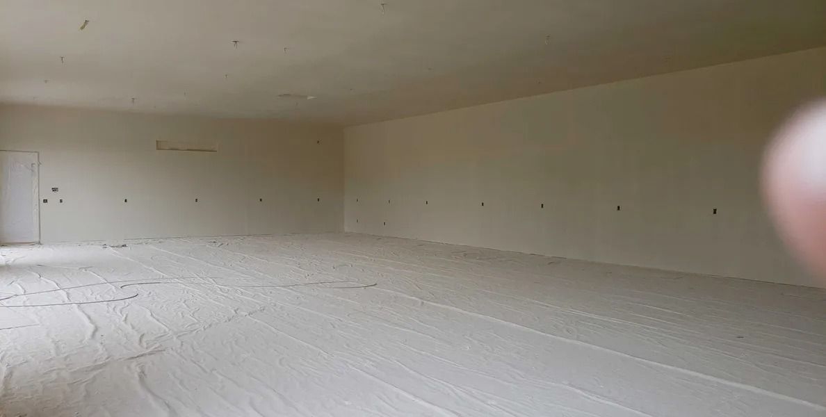 Interior view of a rectangular, light-colored room with textured walls and a slightly angled floor.