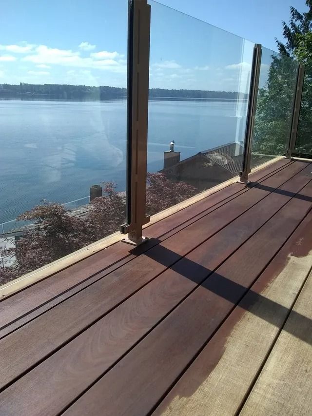 Wooden deck with glass railing overlooking a body of water and distant land under a blue sky.