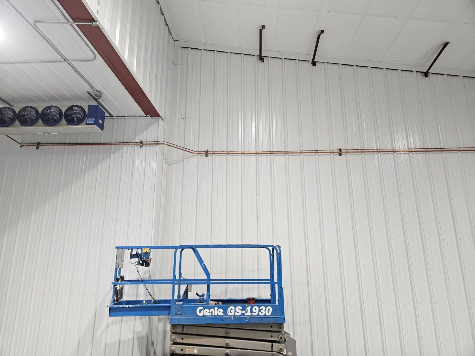 Blue lift inside a white-walled industrial building. Copper wiring runs along the walls.