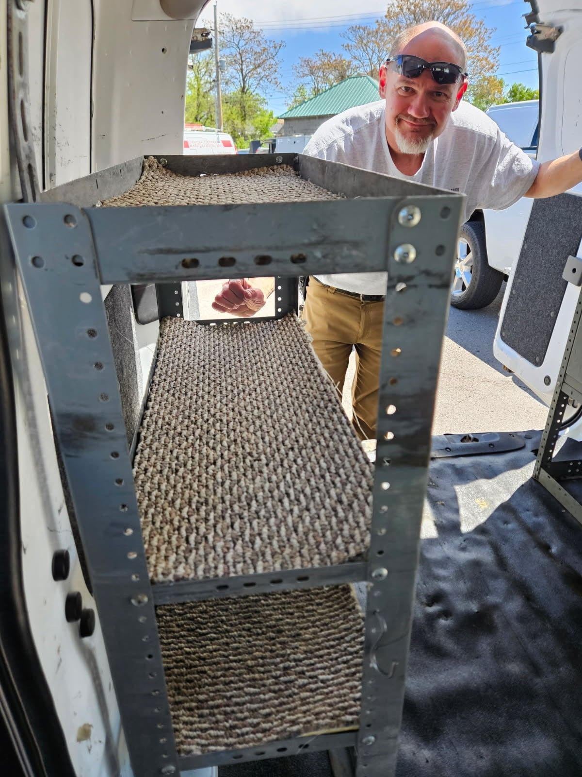 Man smiles while standing inside a van next to a metal shelving unit with woven shelves.