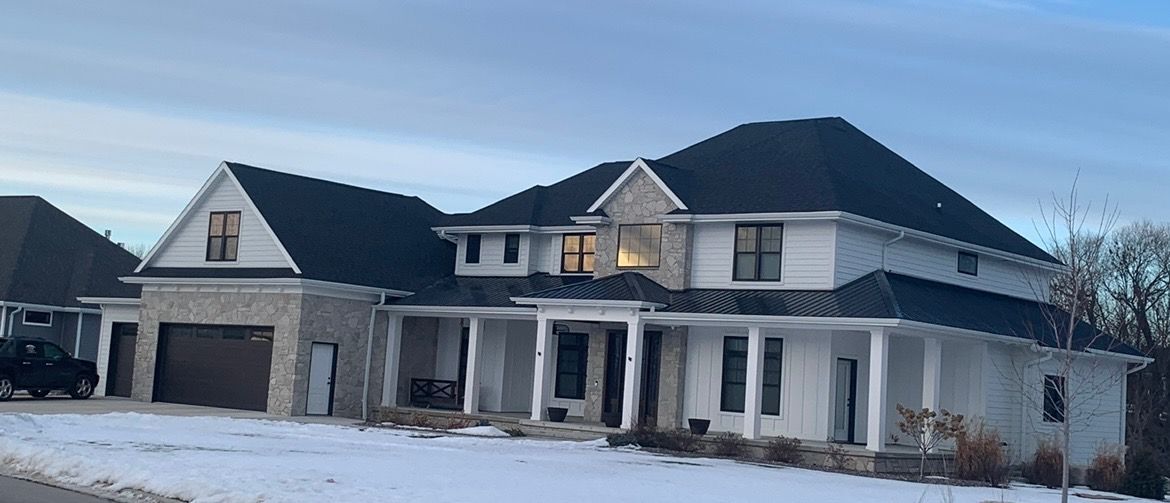 A large white house with a black roof is sitting in the snow.