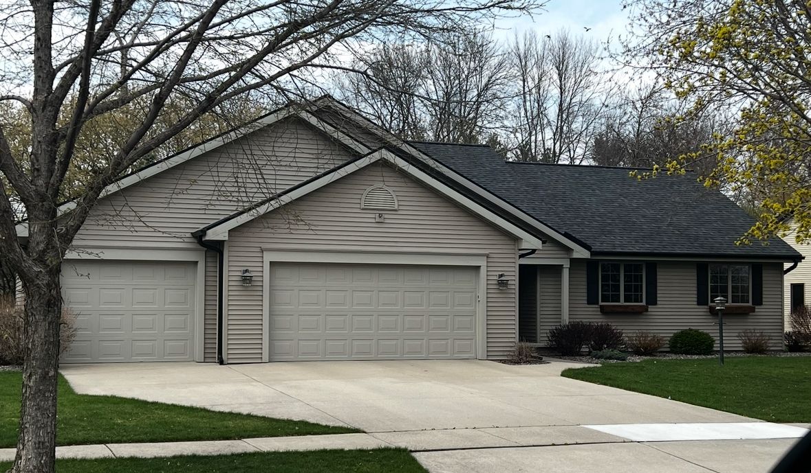 A large house with three garage doors and a tree in front of it.