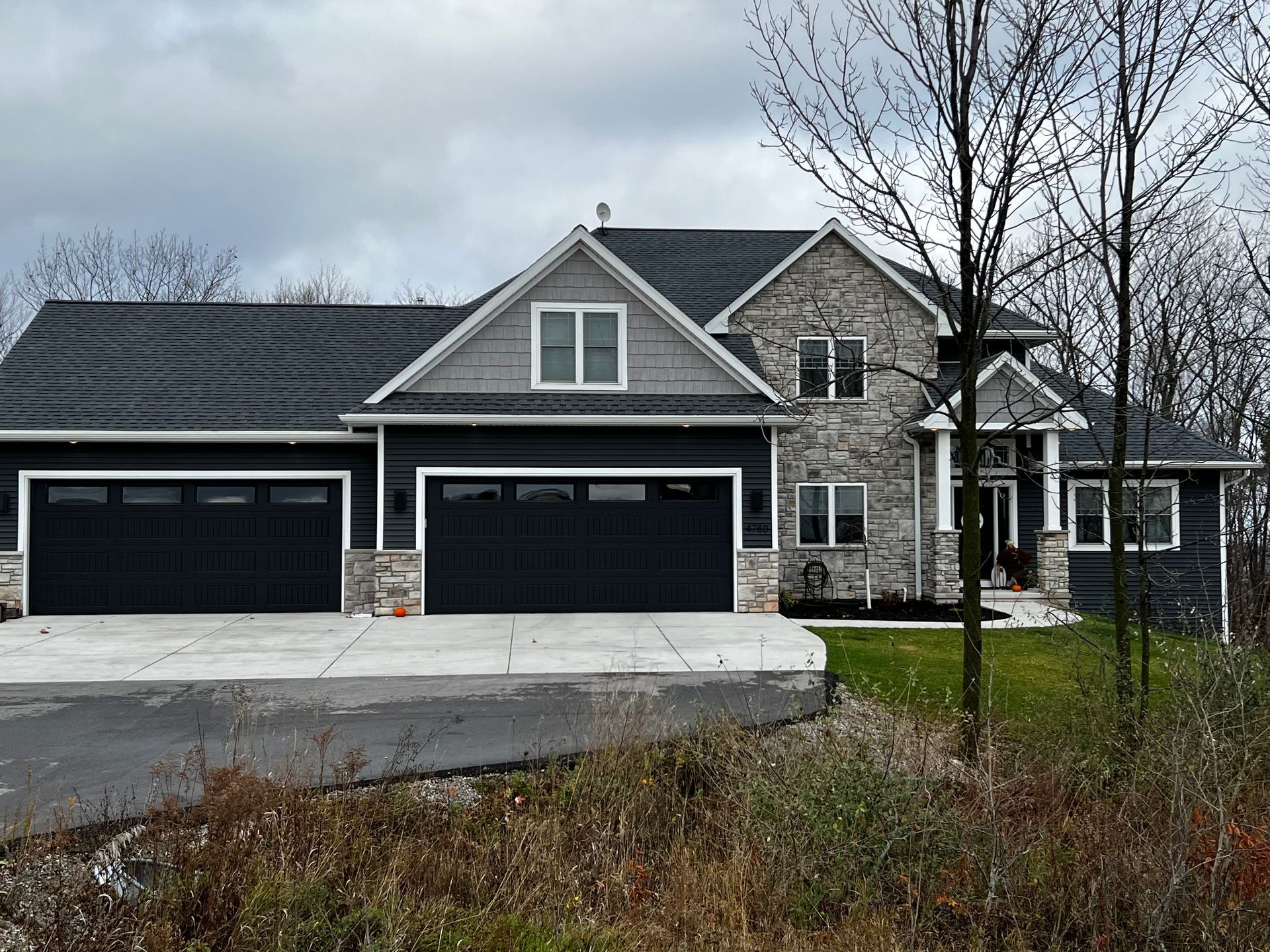 A large house with two black garage doors is sitting on top of a lush green hillside.